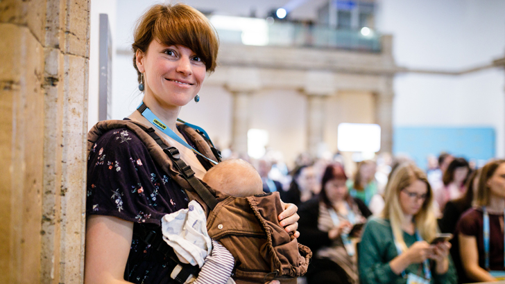 Eine Mutter steht mit Baby in einer Trage bei der Chef:innensache Konferenz 2019